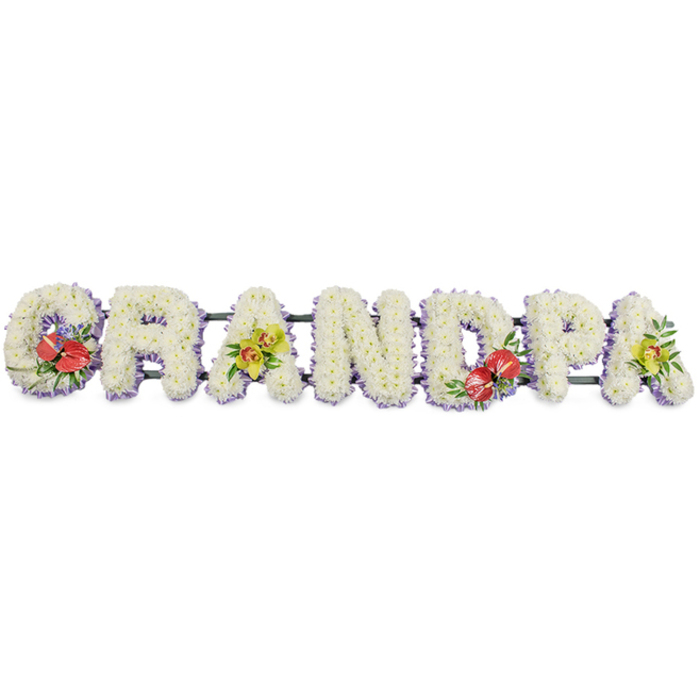A bespoke funeral tribute in the photograph spells out the word "GRANDPA" in bold block capitals, arranged in a single horizontal row so that each letter touches the next, forming one continuous memorial piece. The entire design is set against a bright white background, allowing the clean lines and textures of the flowers to be clearly seen. Every letter has been expertly covered with dense clusters of crisp white chrysanthemums, the small, uniform blooms packed so closely that they form a smooth, cushioned surface suggesting comfort, purity, and calm. A slim band of pale lavender ribbon trims the base of each letter, the muted purple tone gently outlining the shapes and lending a subtle, contemporary finish without overpowering the white flowers. The letters are supported by dark green metal bars, mostly hidden beneath the blossoms, which keep the tribute stable for display at a funeral service or graveside. To add colour and individuality, four letters are accented with carefully placed sprays. On the far left, the 'G' is decorated with a vivid grouping of deep red anthuriums, their distinctive heart-shaped, glossy petals and upright yellow spadices surrounded by rich green foliage. The first 'A' carries an arrangement of graceful yellow-green orchids with elegant petals and buds, softened with fresh leafy greens. Near the centre, the 'D' echoes the 'G' with another cluster of red anthuriums and foliage, creating balance along the tribute. The final 'A' on the right repeats the orchid theme, bringing the design full circle. This GRANDPA floral tribute would be at home in a Kensal Green chapel or cemetery setting, a dignified, personalised expression of love and respect for a cherished grandfather.